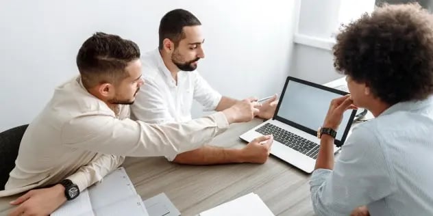 A group of three men in deep discussion while reviewing content on a laptop screen.