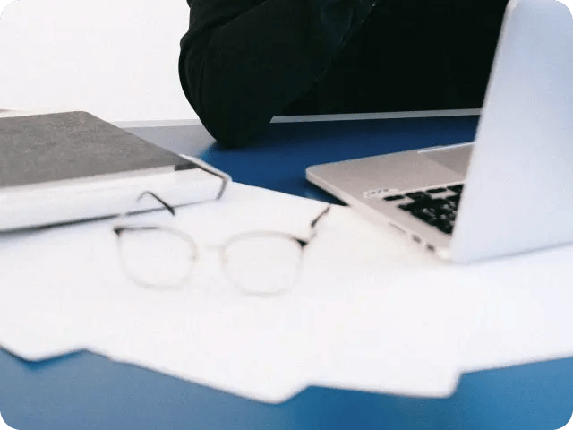 A close-up of an organized workspace featuring a laptop, a notebook, and a pair of glasses on a desk.
