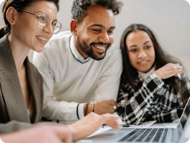 A collaborative group of two women and one man smiling as they review content together on a laptop.